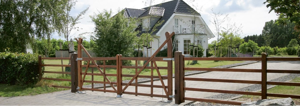 Eine Reihe von Hartholztoren blockiert die Auffahrt zu einer schönen Villa mit weißen Wänden und schwarzem Ziegeldach | Poda Zaun